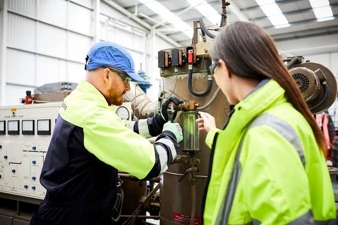 Industrial equipment inspection, two workers in high-visibility clothing, workshop machinery, equipment controls, maintenance activity